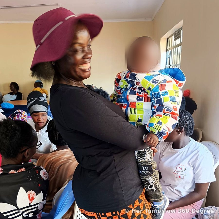 A smiling woman holds up a toddler in a colourful jacket during the session